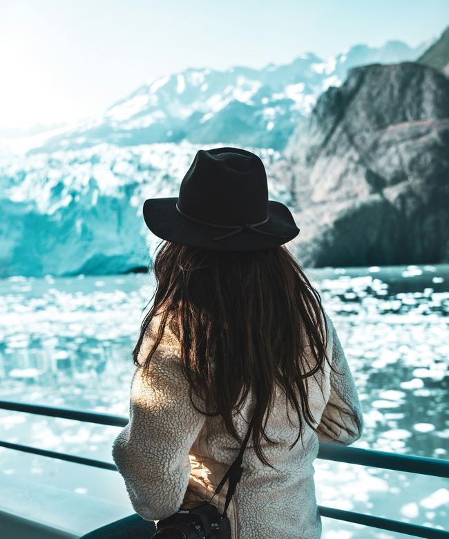 Voyageuse au chapeau noir face au glacier, voyage solo sur mesure
